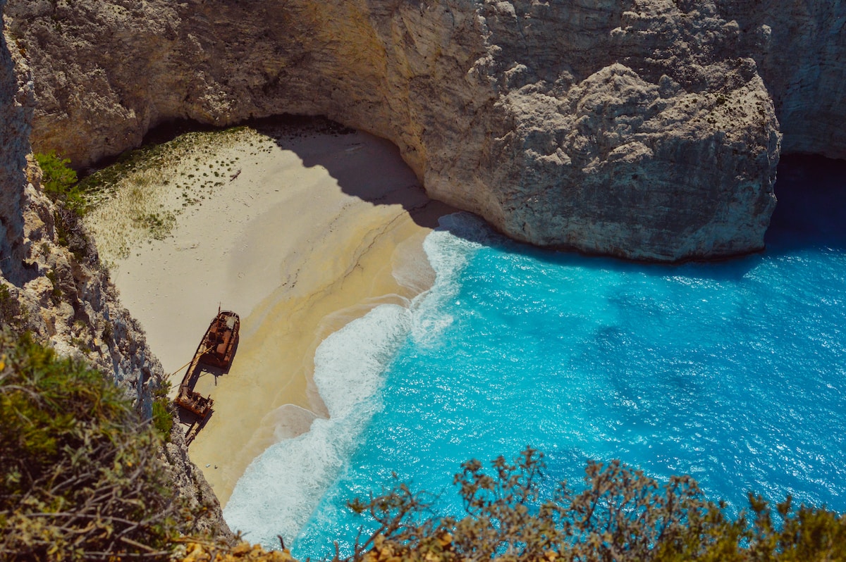 wrecked ship on shore near cliff during daytime - Santorini's Beach