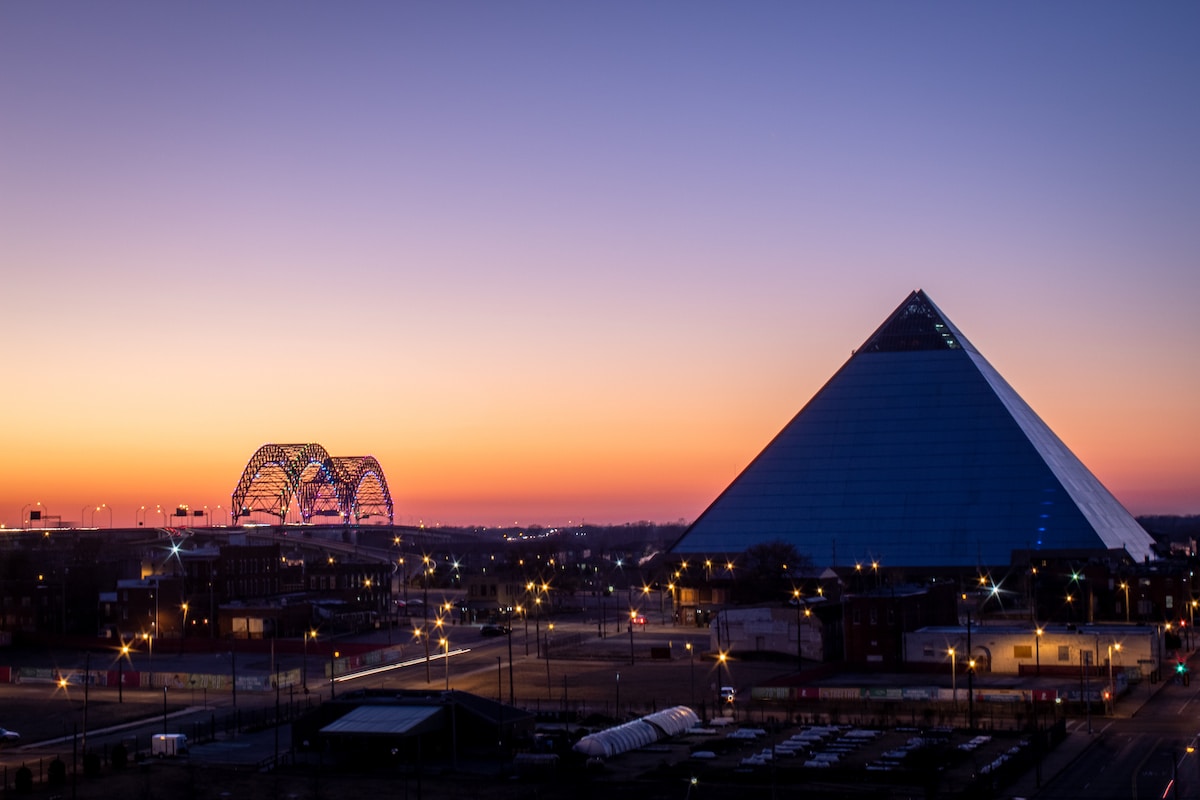 a sunset view of a large pyramid with a ferris wheel in the background - Memphis
