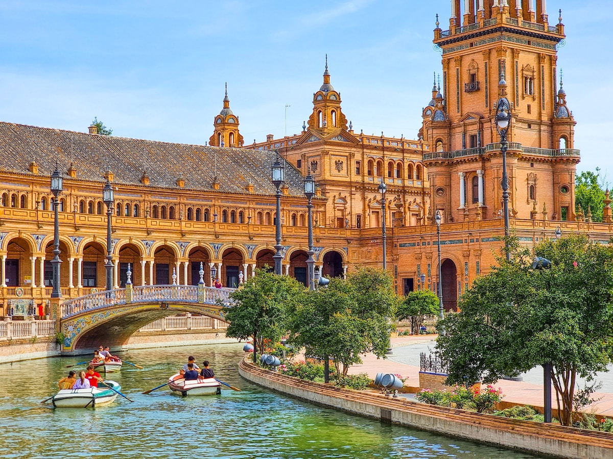 a group of people in a boat in a river in front of a large building - Seville
