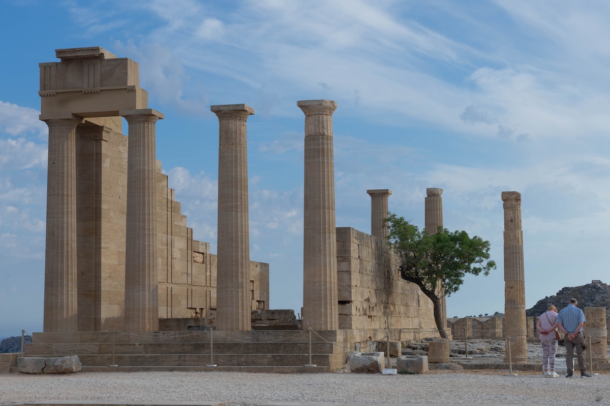 a couple of people standing in front of some stone pillars Acropolis' Monuments