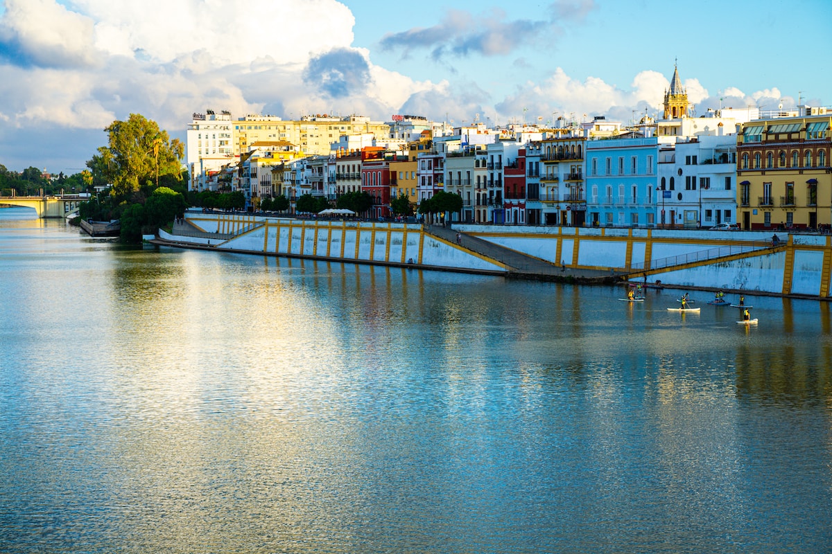 a body of water with buildings in the background - Guadalquivir River, Seville, Spain
