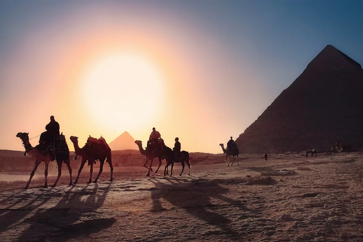 five persons riding camels walking on sand beside Pyramid of Egypt - Cairo Egypt Travel Guide
