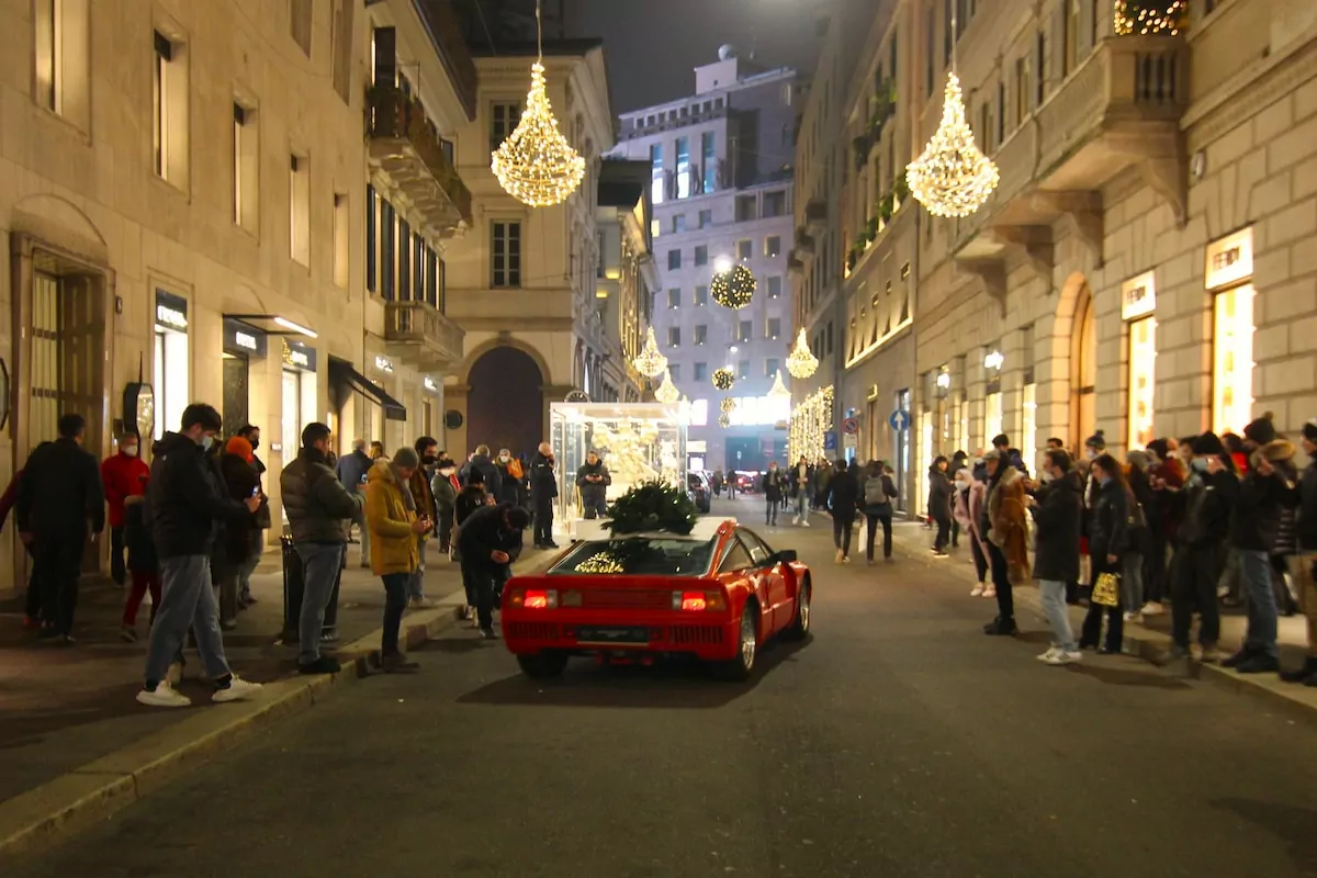 a red sports car on a street with people walking around - Via Monte Napoleone