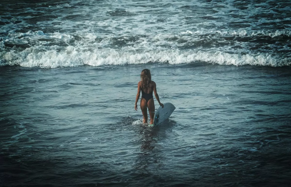 woman in black bikini surfing on sea waves during daytime in Canggu beach, Bali