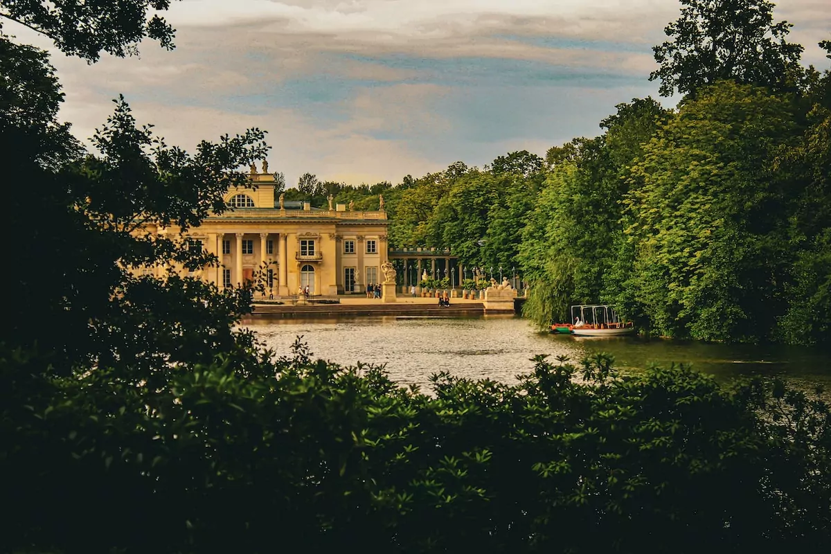 a large building sitting on top of a lake surrounded by trees - Łazienki Park