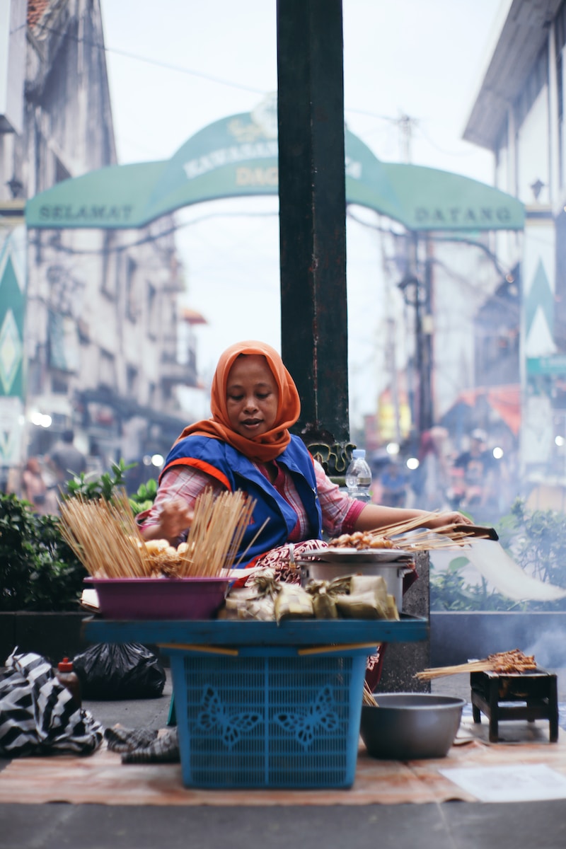 woman in blue and brown hijab sitting on red plastic crate - Yogyakarta